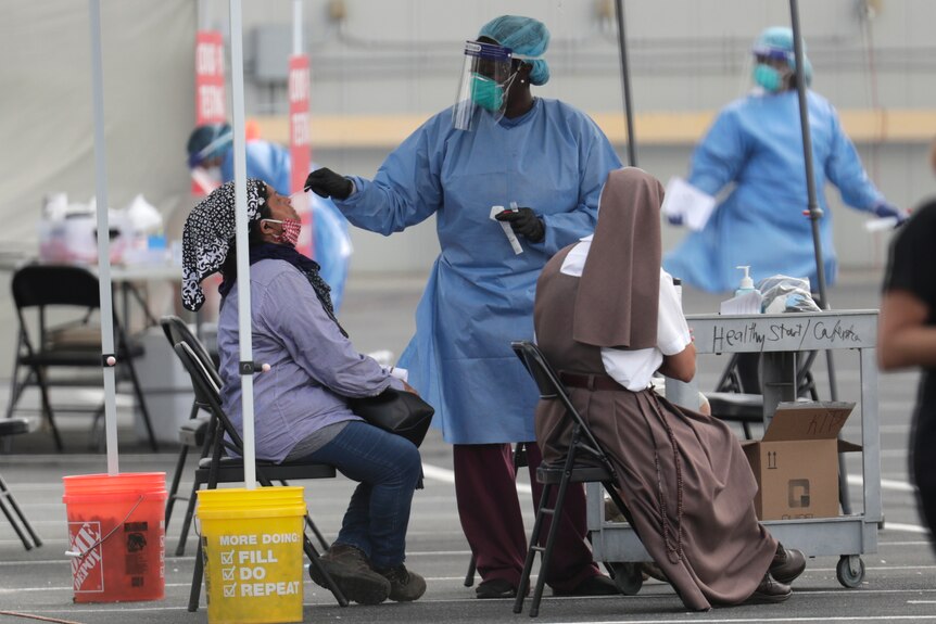 A woman in full PPE administers a coronavirus test to another woman at an outdoors testing site.