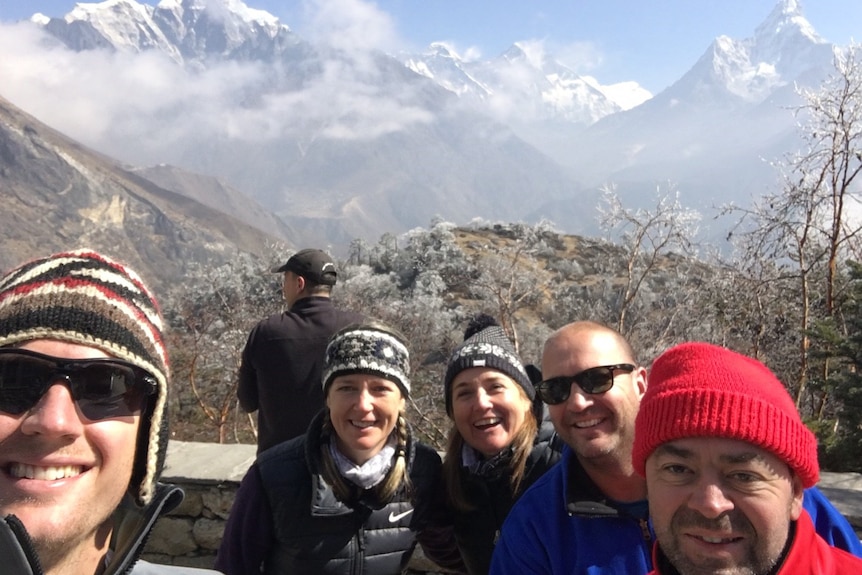 Four people smiling with a Himalayan mountain range behind them