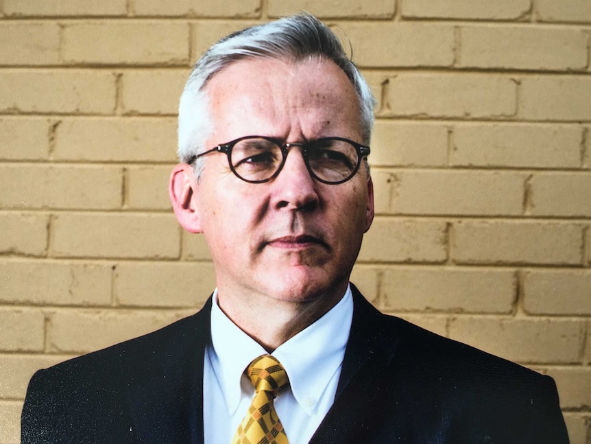 John Blaxland looks speculative in front of a brick wall.