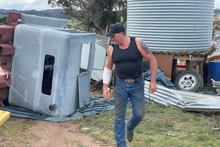 A man walks in front of a toppled trailer.