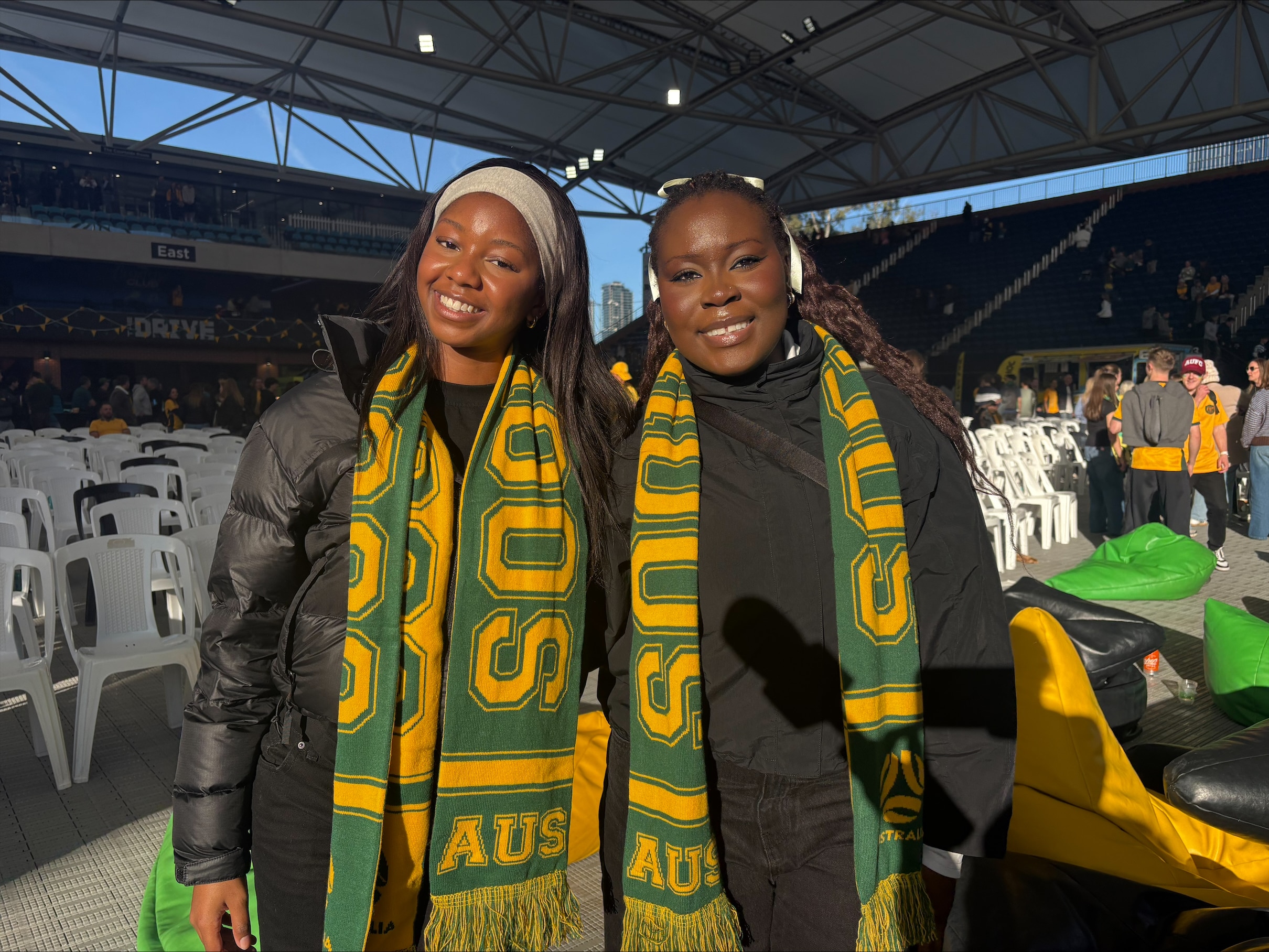  Two women smile while wearing green and gold scarves.
