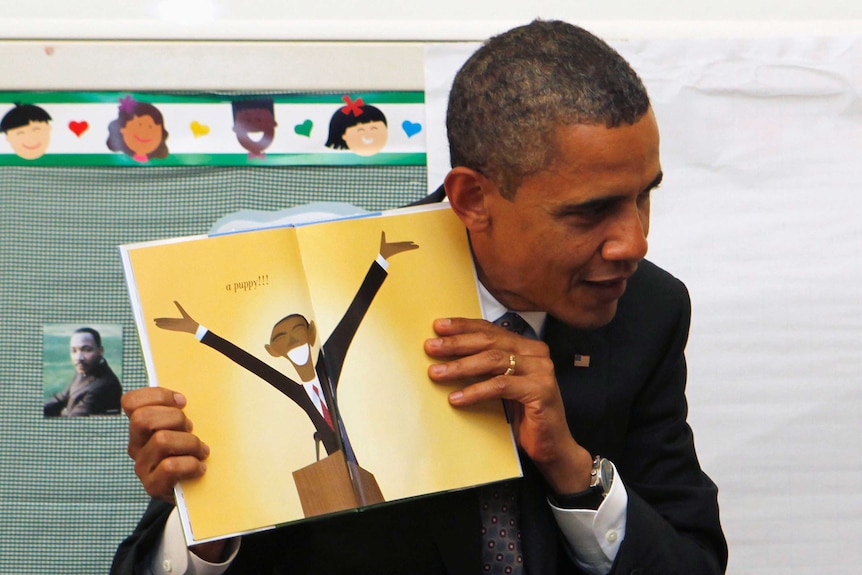 US President Barack Obama holds up a book with a cartoon of himself.