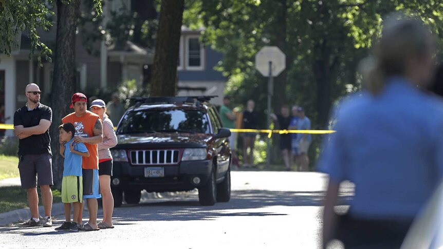Police and residents are photographed on a suburban tree-lined street near a cordoned-off crime scene.
