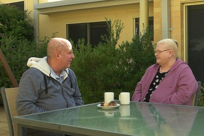 a man and a woman sitting outdoors drinking outof cups