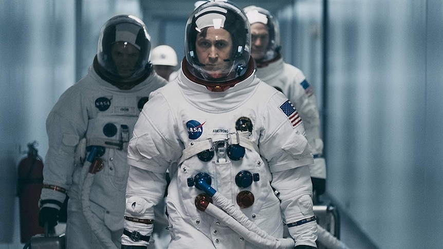 Lukas Haas, Ryan Gosling, and Corey Stoll walking down a corridor in spacesuits in a scene from First Man (2018)