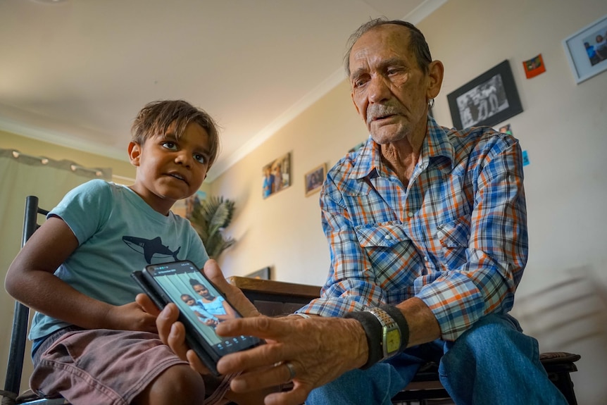 A man in his 80s and a young boy sit together in a room, looking at older photos.