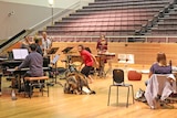 Pianist and other musicians and Indigenous dancer performing around a kangaroo skin on floor of auditorium.