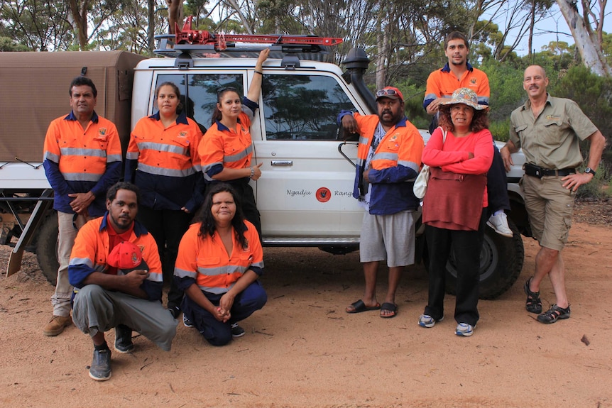 A group of indigenous rangers stand in front of a four wheel drive vehicle with group logo