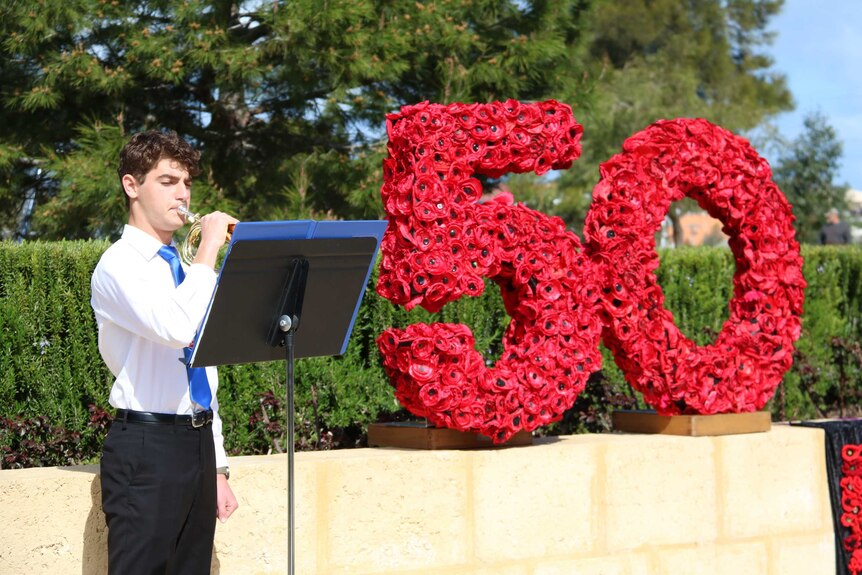 A lone bugler stands in front of a memorial showing 50 years, woven out of poppies.