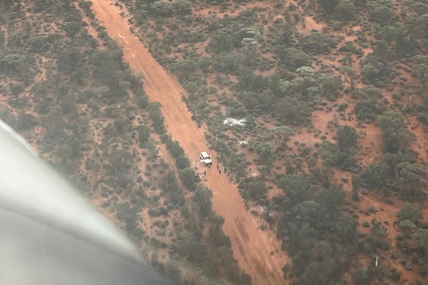 Photograph through plane window of people bogged in the outback on dirt road located by aerial search. 