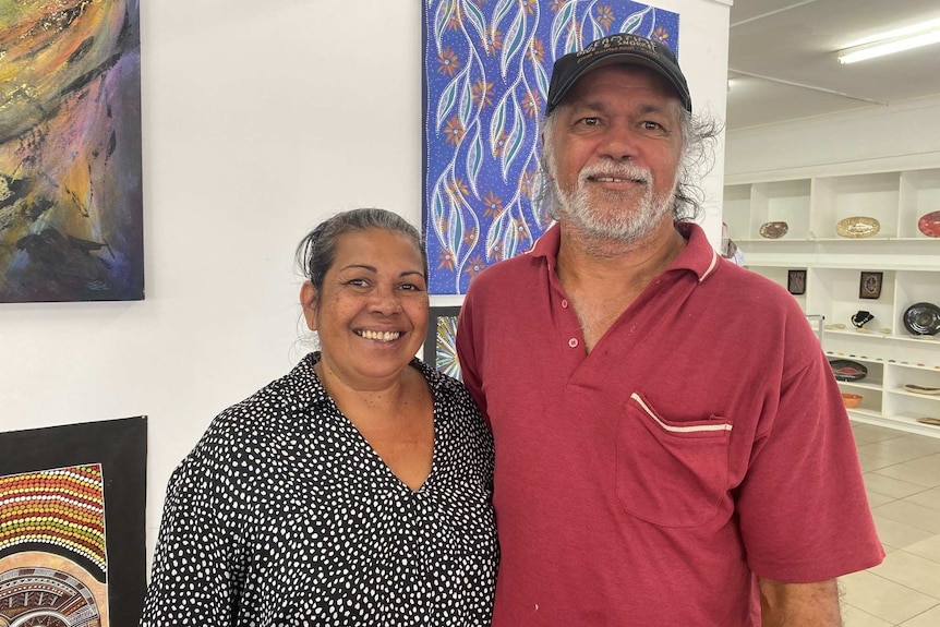 Smiling Indigenous woman and man standing in front of artworks