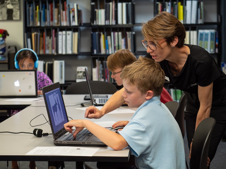 A female teaching assisting a male student using a laptop computer.