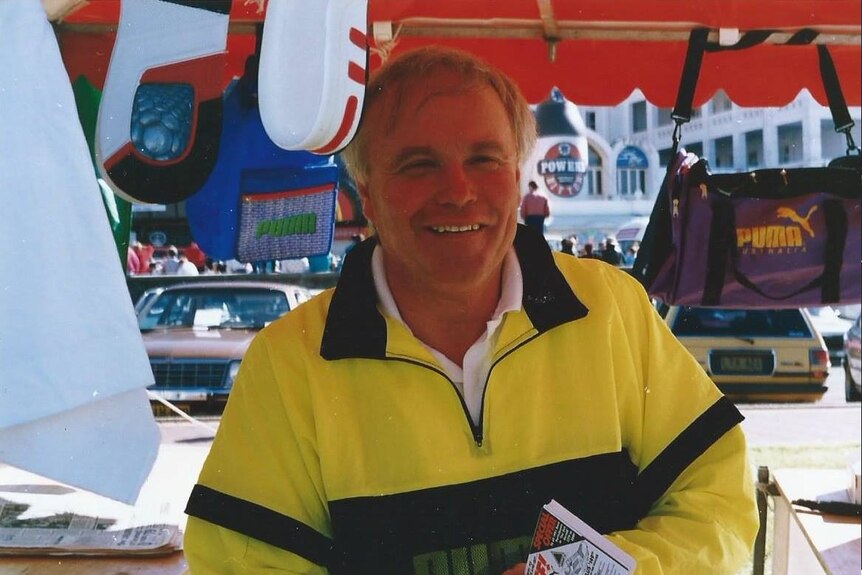 An older man wearing a tracksuit and smiling.