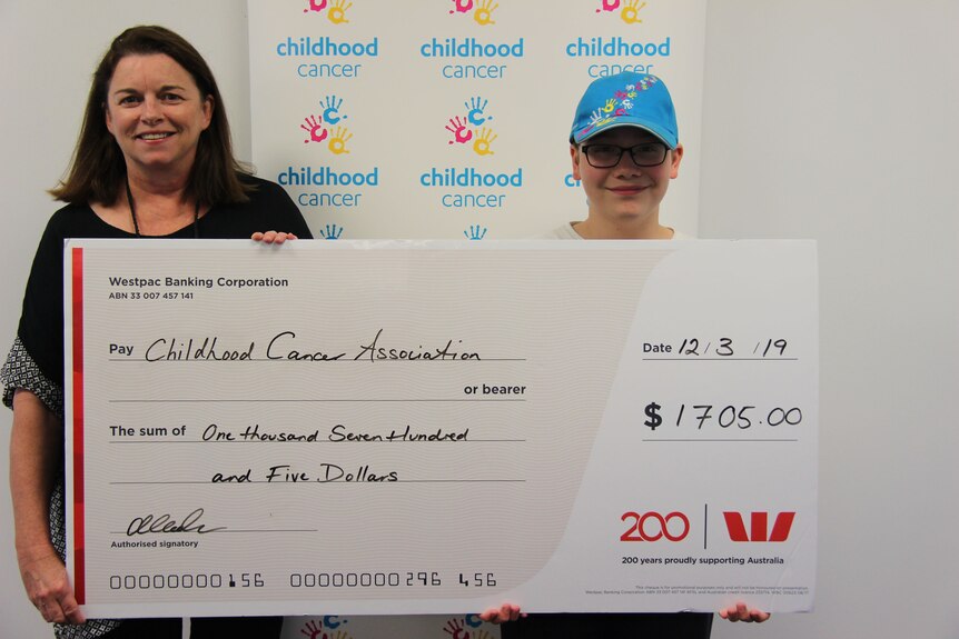 Sam stands with Childhood Cancer Association CEO, Cath O’Loughlin with a large novelty cheque for $1,705.