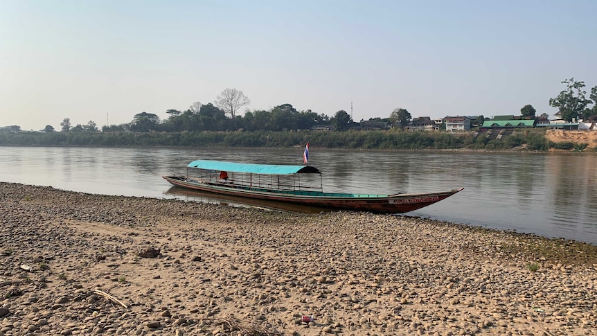 A fishing boat is parked up on the bank of the river, where the water level is drastically low.