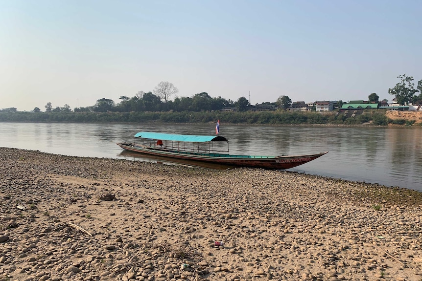 A fishing boat is parked up on the bank of the river, where the water level is drastically low.