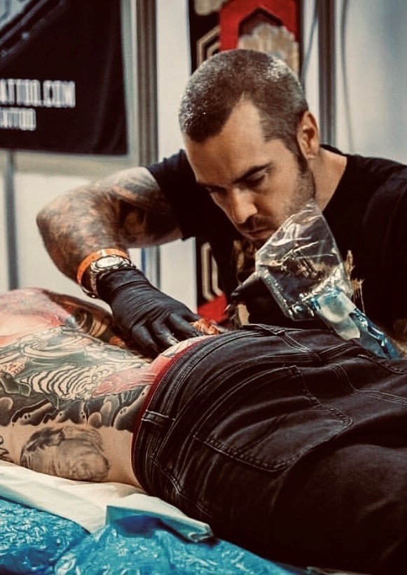 A man works on a tattoo on the lower back of a customer. 