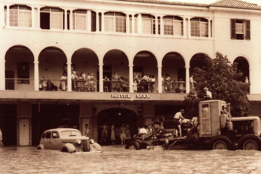 Old photo showing a flooded street in Moree, and people moving belongings from the water.