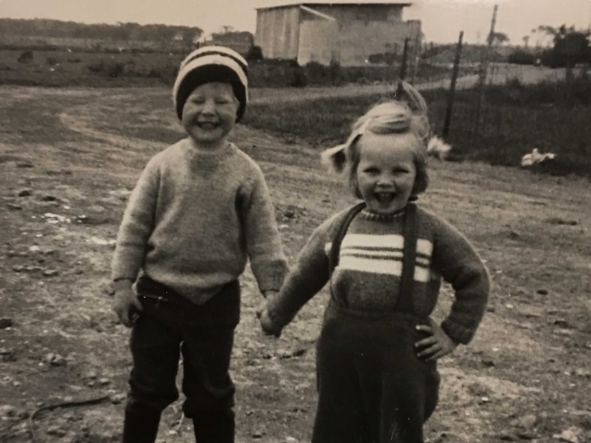 Black and white grainy photograph depicting two grinning children holding hands in a farmyard setting