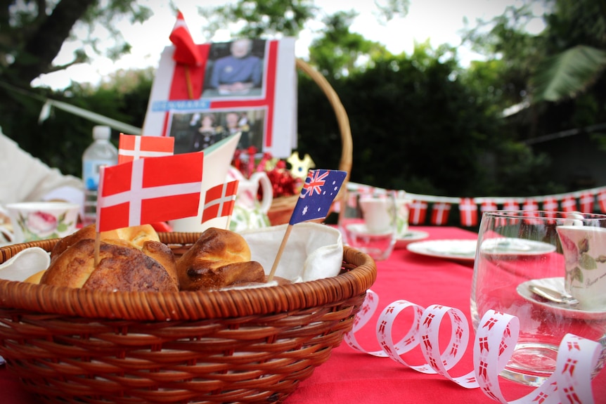 A basket of baked goods with small Danish and Australian flags on toothpicks, a red table cloth and Danish flag bunting
