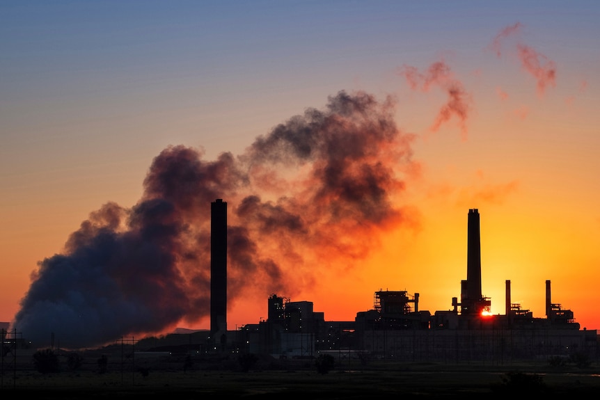 Il fumo che esce da una centrale elettrica a carbone è oscurato dalla luce del sole del mattino.