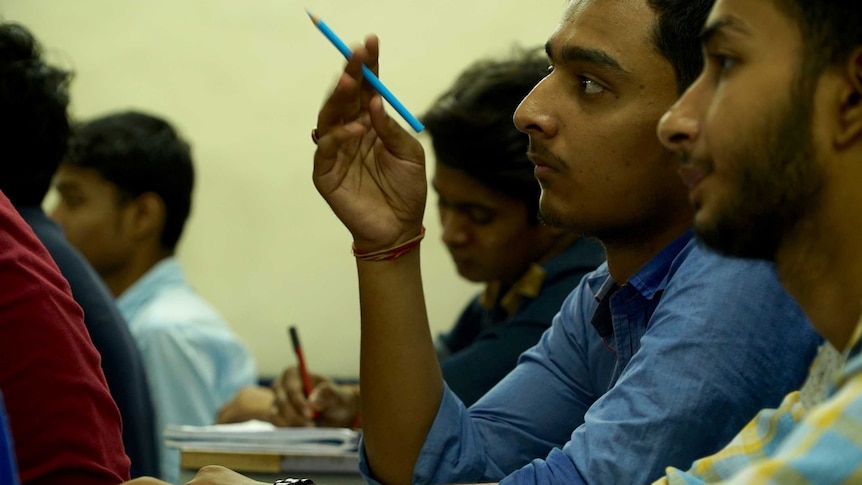 Close-up of Indian student in classroom holding pencil.