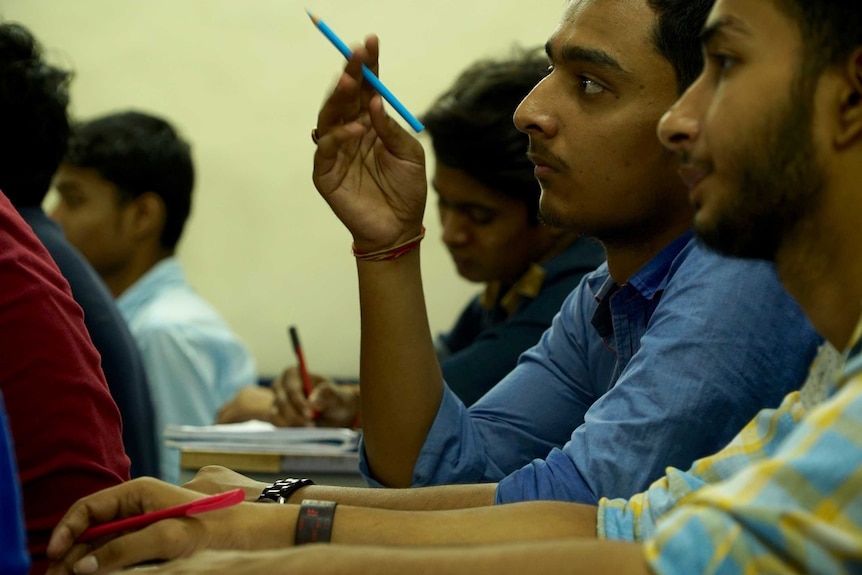 Close-up of Indian student in classroom holding pencil.