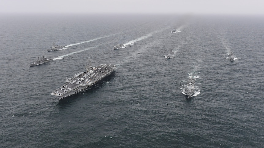 A series of naval ships in formation in the sea. 
