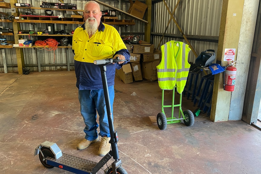 A man in hi-vis with a beard holds an electric scooter in a workshop
