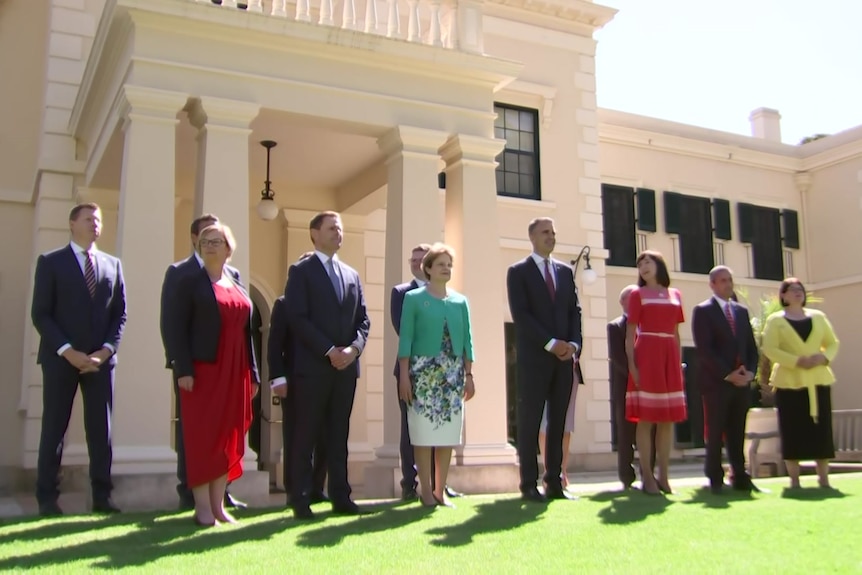 A group of people in suits and dresses in front of an old house