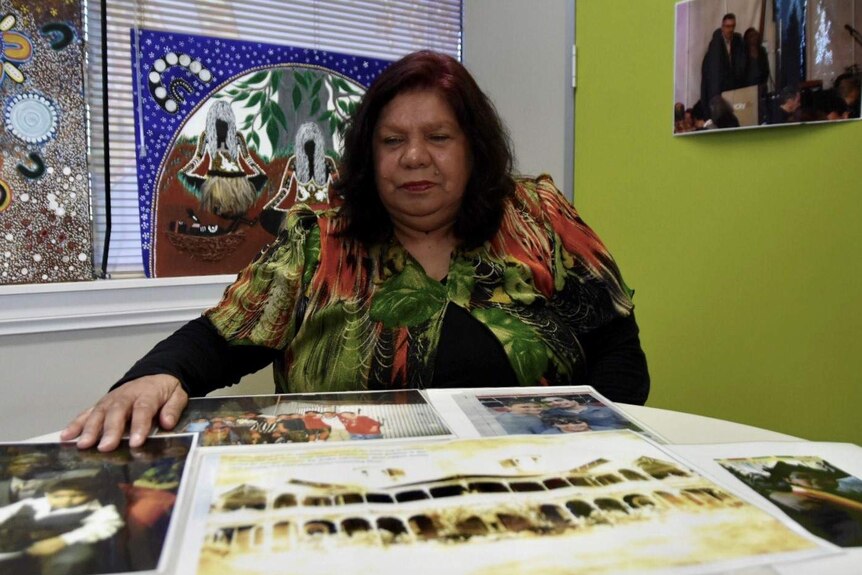 Lyn Austin, a member of the Stolen Generations, sits at a table looking at historical family photos.