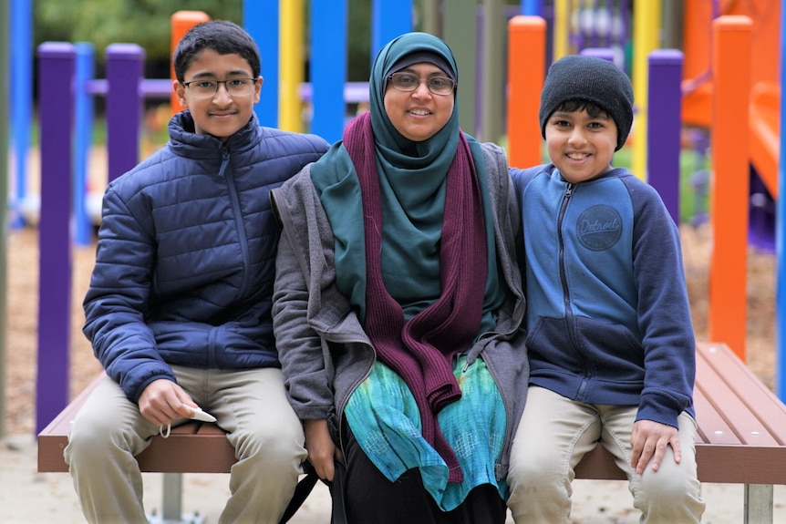 A mother sitting between her sons in a playground