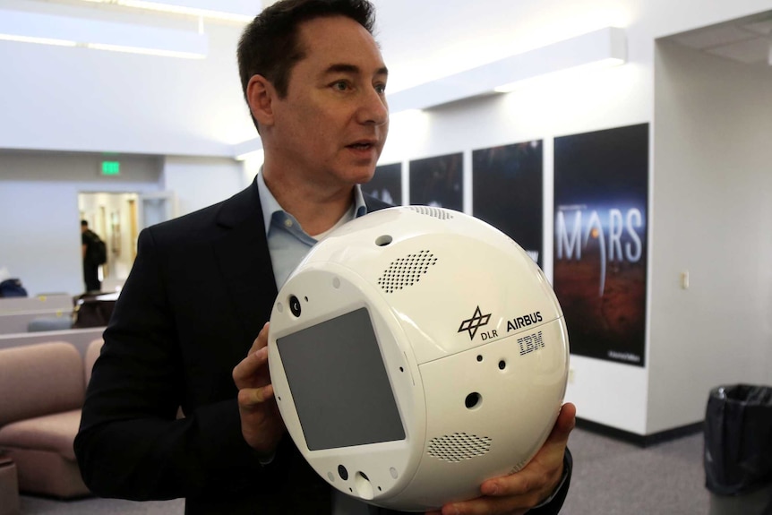 A man in a suit holds a round, white robot, which carries IBM branding.