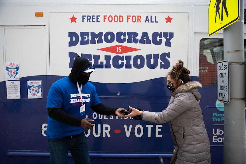 A volunteer and voter standing in front of a food truck, passing food between each other.