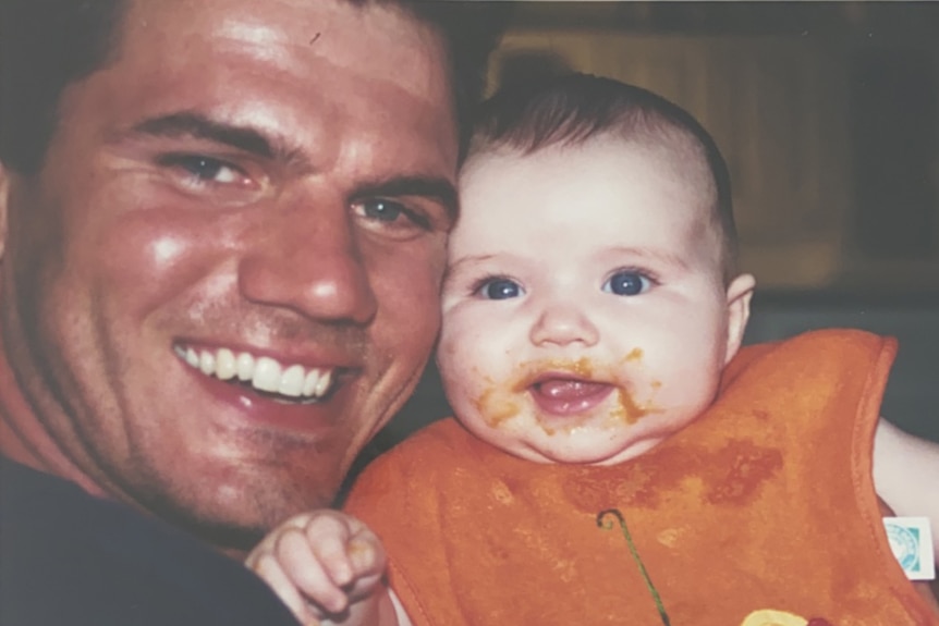 A young dad smiles with his baby whose covered in food.
