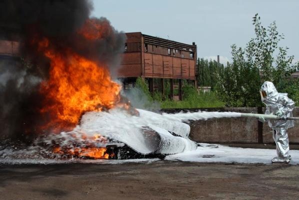 person in silver hazmat suit spraying fire with white foam from a hose