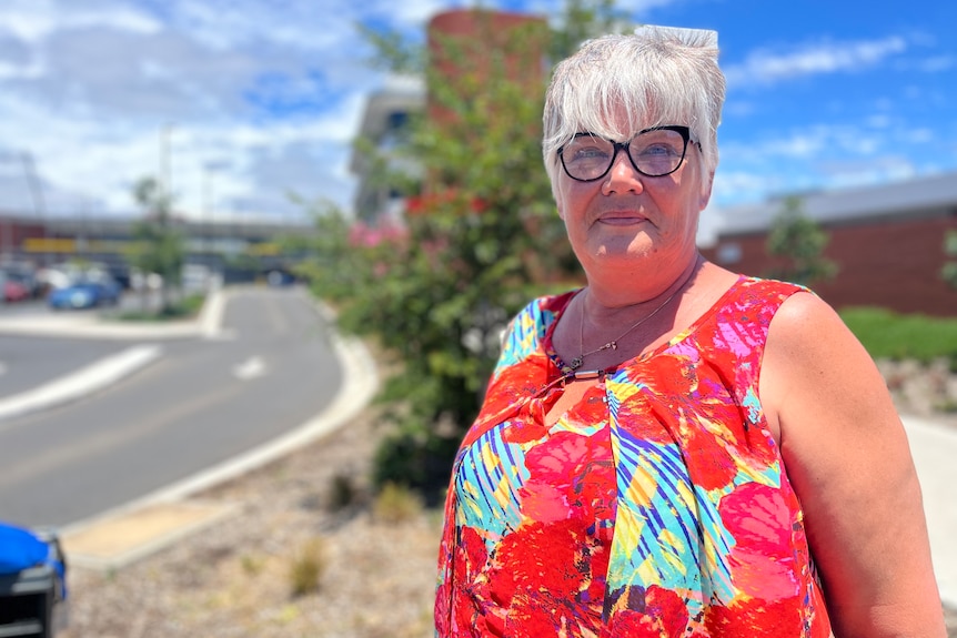 A middle-aged woman in a colourful top and glasses standing by a road