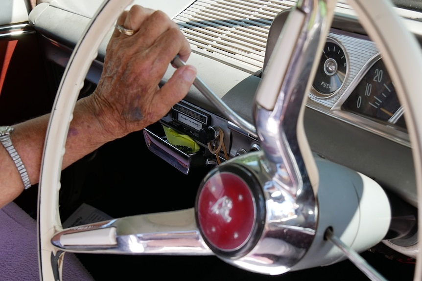 Older woman's hand on stick shift of vintage holden car steering wheel
