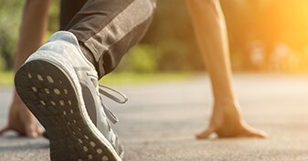 Close up of a person poised, about to run. An up-turned sneaker in the foreground, with hands pressed on the ground behind.