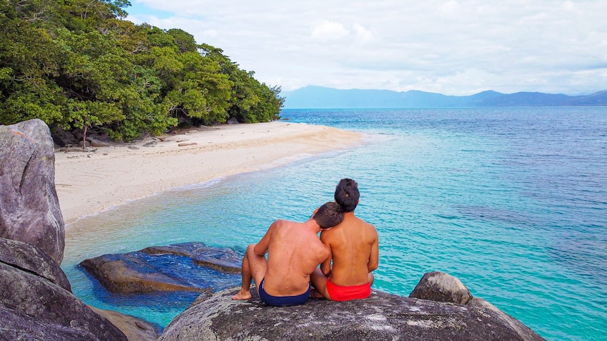 Gay couple sitting close together on a rock looking out at the ocean.