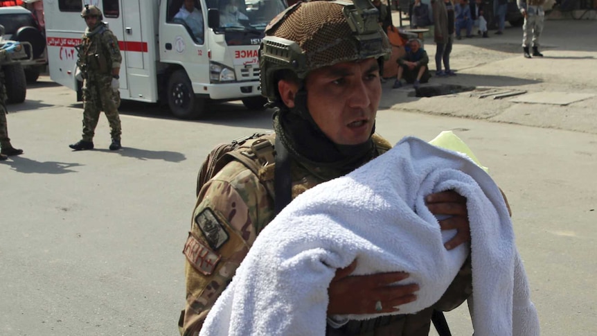 An Afghan security officer carries a baby after gunmen attacked a maternity hospital.