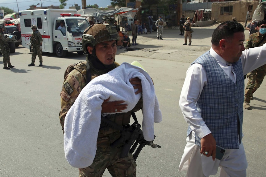 An Afghan security officer carries a baby after gunmen attacked a maternity hospital.