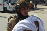 An Afghan security officer carries a baby after gunmen attacked a maternity hospital.