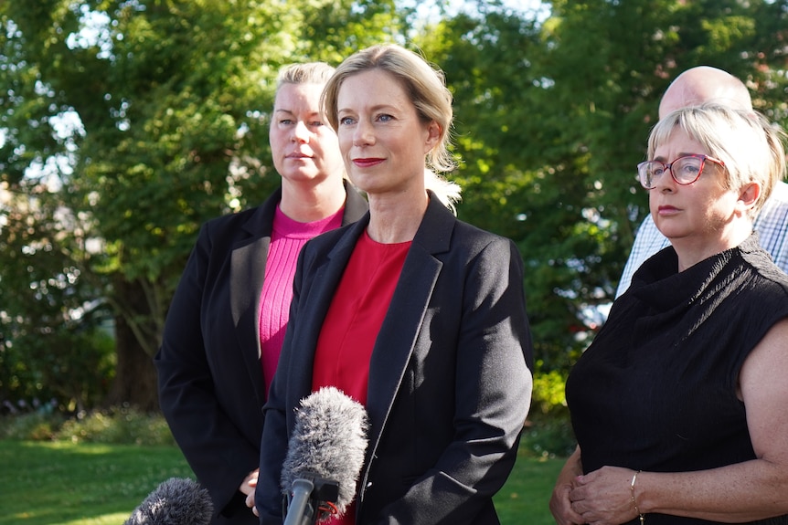 Three women, all wearing black, stand in a row. 