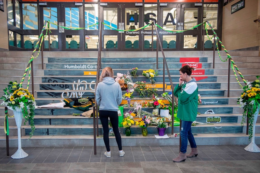 Two women are seen standing by the stairway entrance of the hockey arena where flowers and notes are placed.