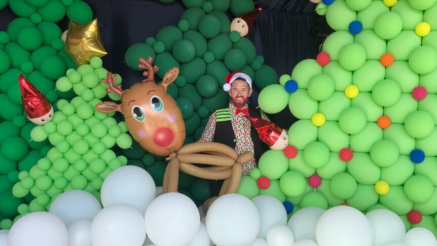 Man standing with Christmas trees made out of balloons.