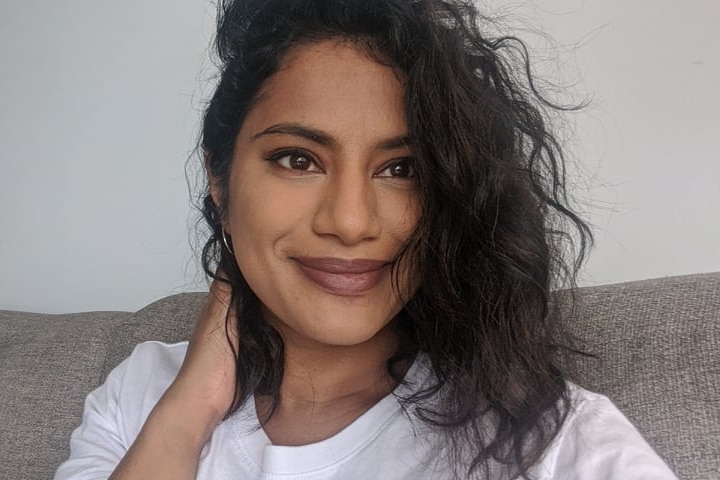 Selfie of Lakshmi Nadarajamoorthy smiling on a grey couch