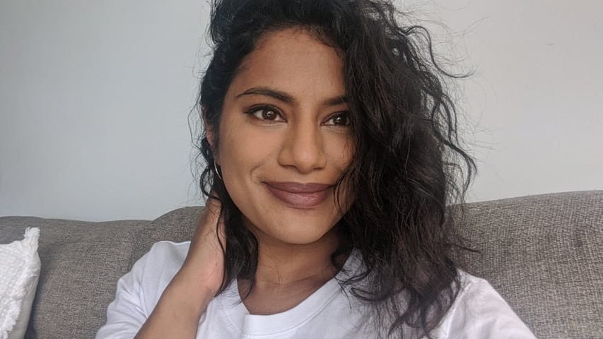 Selfie of Lakshmi Nadarajamoorthy smiling on a grey couch, in a story about hair rituals connecting people to culture and family