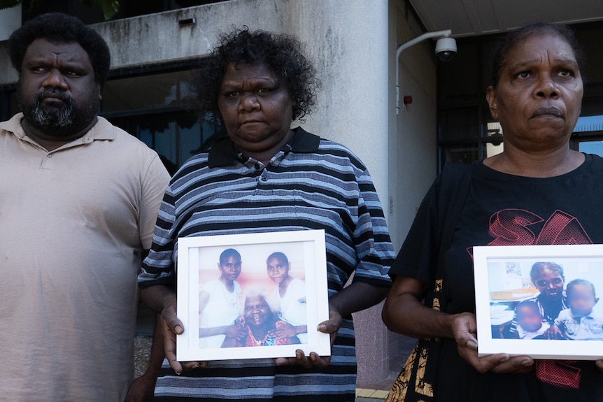 An Aboriginal man and two Aboriginal women standing outside courthouse holding framed pictures of relative