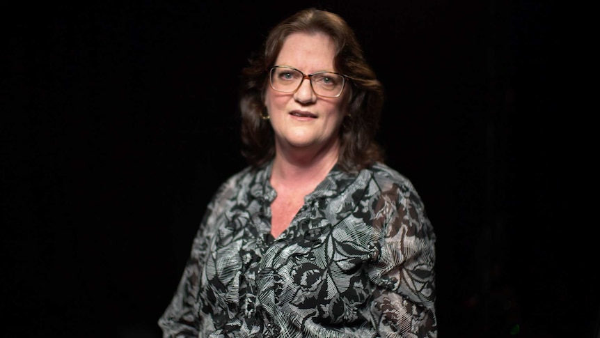 MCU of Bernadette Quigley wearing a black and grey blouse in front of a black background